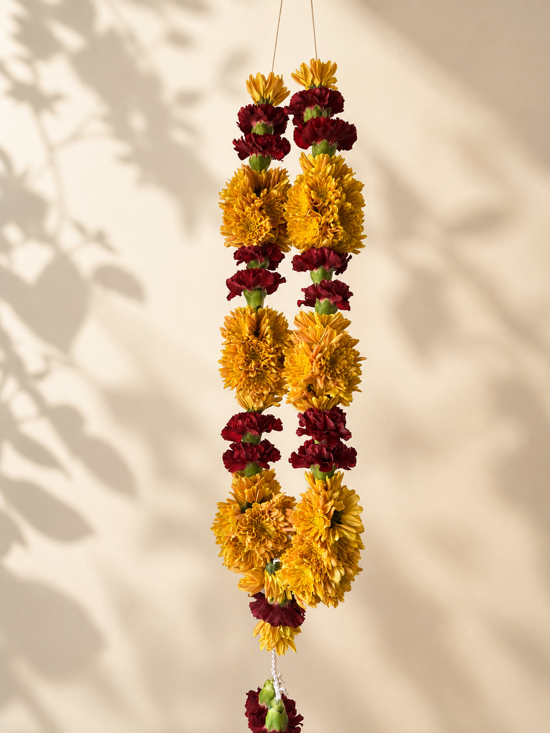 Yellow marigold and burgundy celebration mala on ivory leaf-shadow backdrop