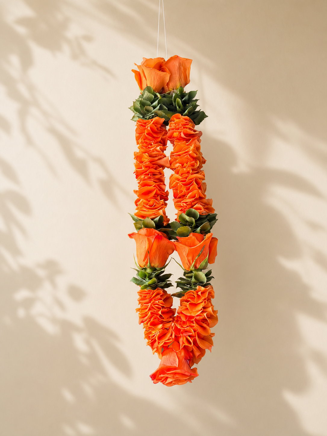 Orange rose and green foliage hanging garland on clean ivory leaf-shadow backdrop