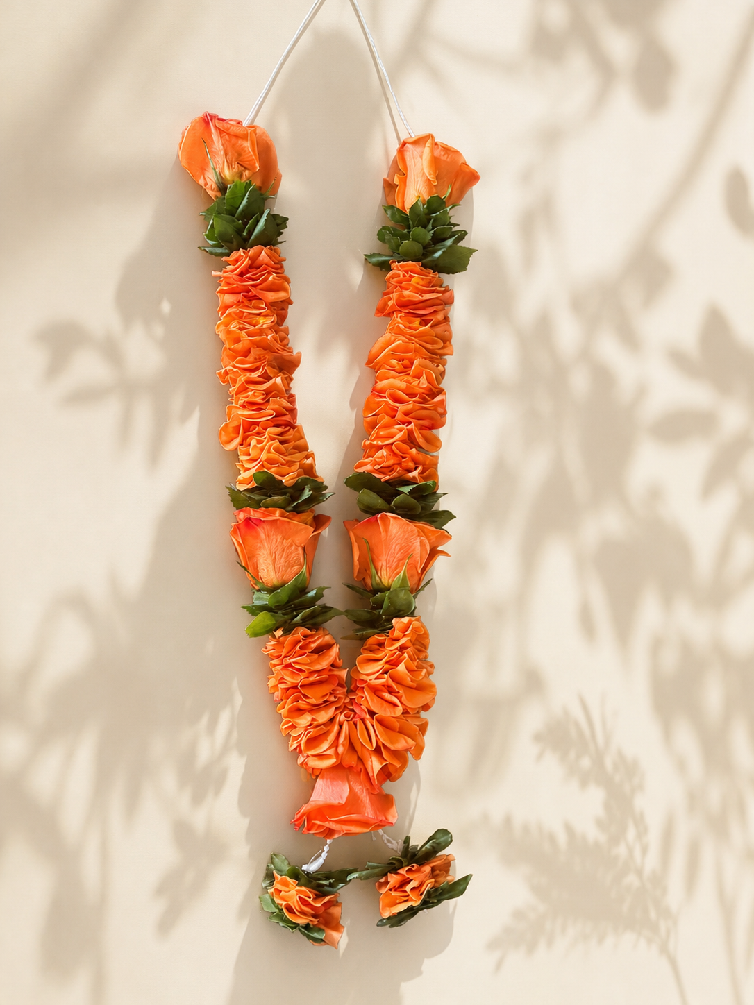 Orange rose and green foliage garland pair on clean ivory leaf-shadow backdrop