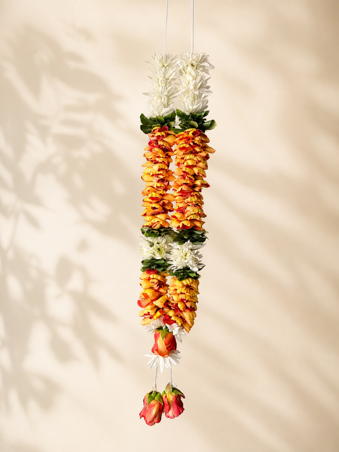 Orange rose petal and white daisy hanging garland with pearl tassels on ivory leaf-shadow backdrop