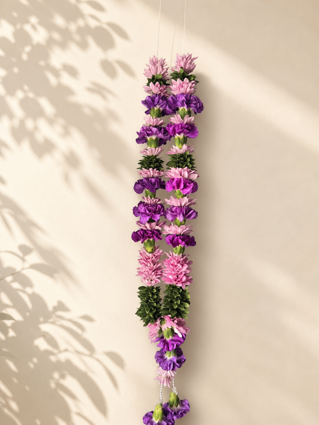 Purple and pink floral welcome garland on ivory leaf-shadow backdrop