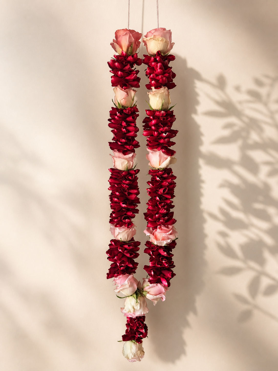 Ruby petal and blush rose hanging mala on ivory leaf-shadow backdrop