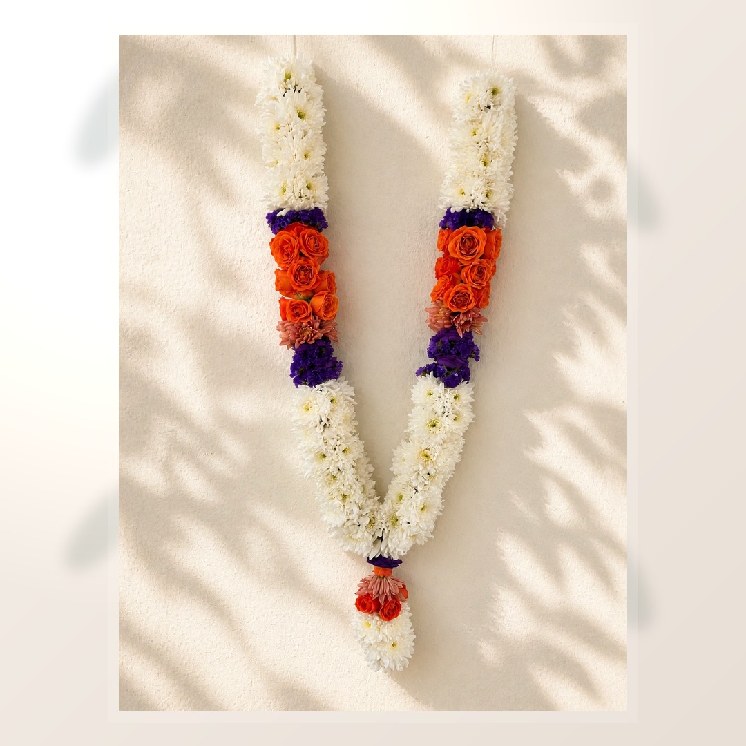 White floral garland with orange roses and purple accent flowers on a warm ivory leaf shadow background