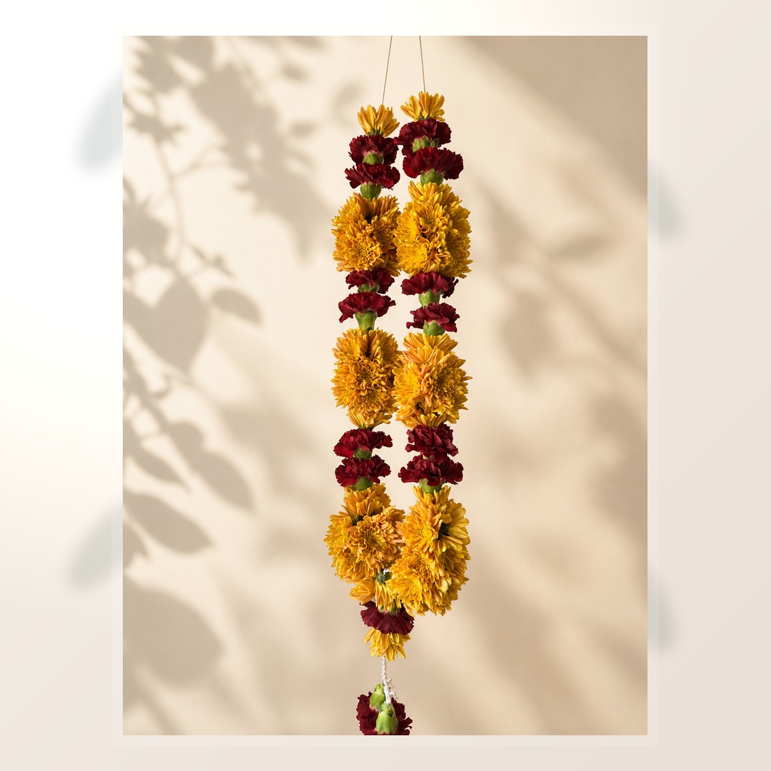 Yellow marigold and burgundy celebration mala on ivory leaf-shadow backdrop