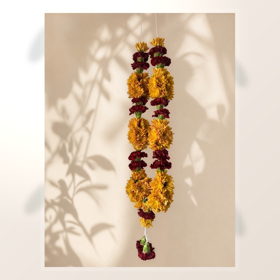 Full length marigold and burgundy celebration garland on ivory leaf-shadow backdrop