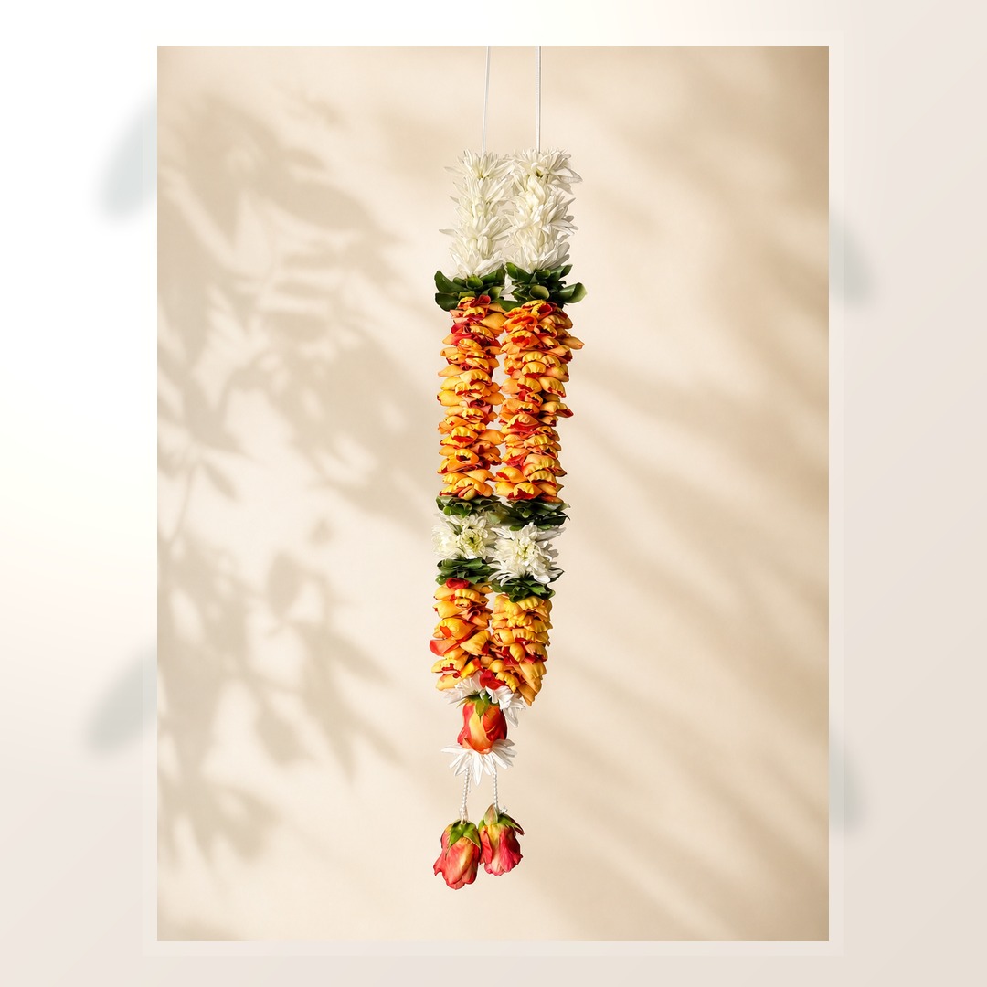 Orange rose petal and white daisy hanging garland with pearl tassels on ivory leaf-shadow backdrop