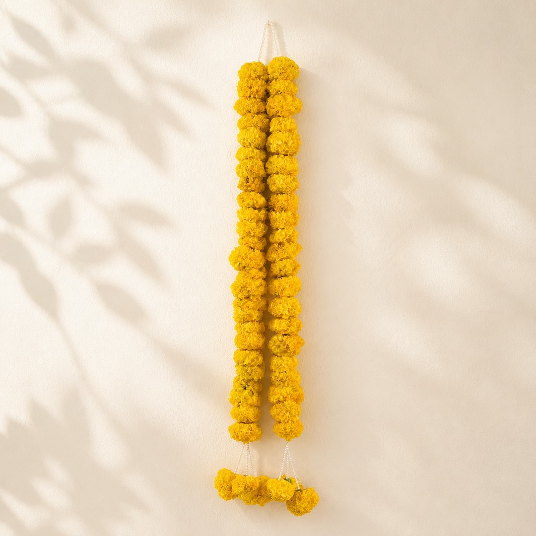 Golden yellow marigold garland with pearl loop on a warm leaf shadow background