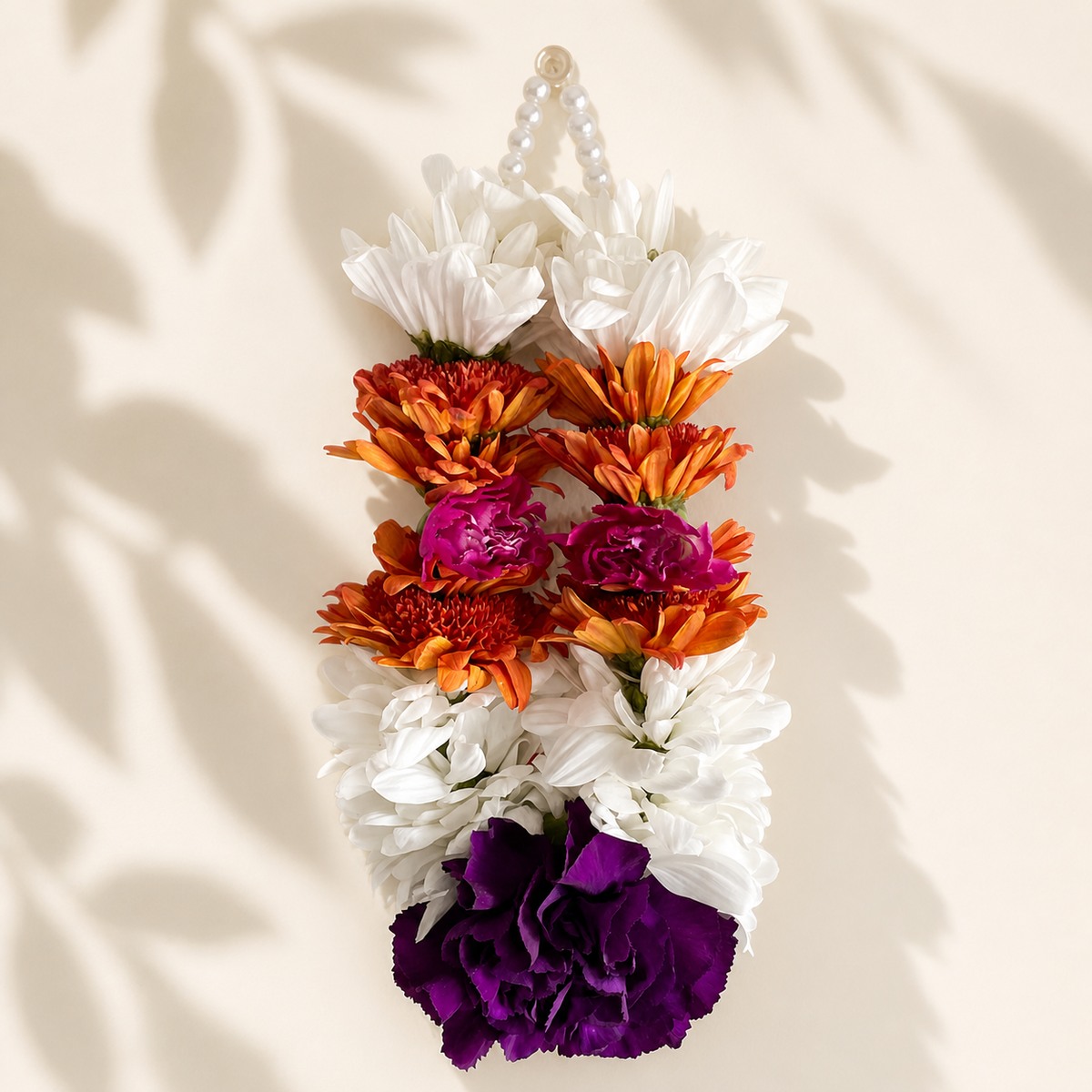 Close view of autumn daisy orchid hanging garland on warm ivory leaf-shadow backdrop