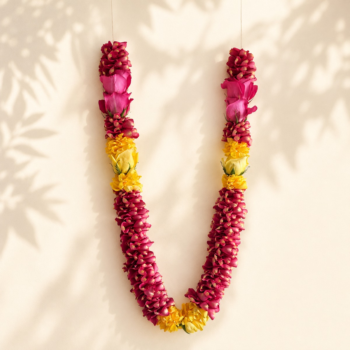 Pink and yellow rose garland full view on warm ivory leaf-shadow backdrop