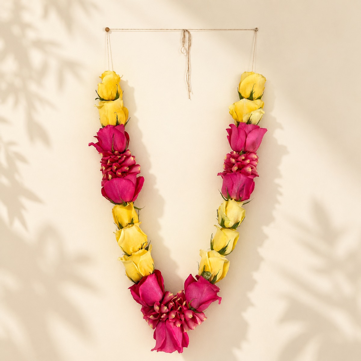 Pink and yellow rose garland detail view on warm ivory leaf-shadow backdrop