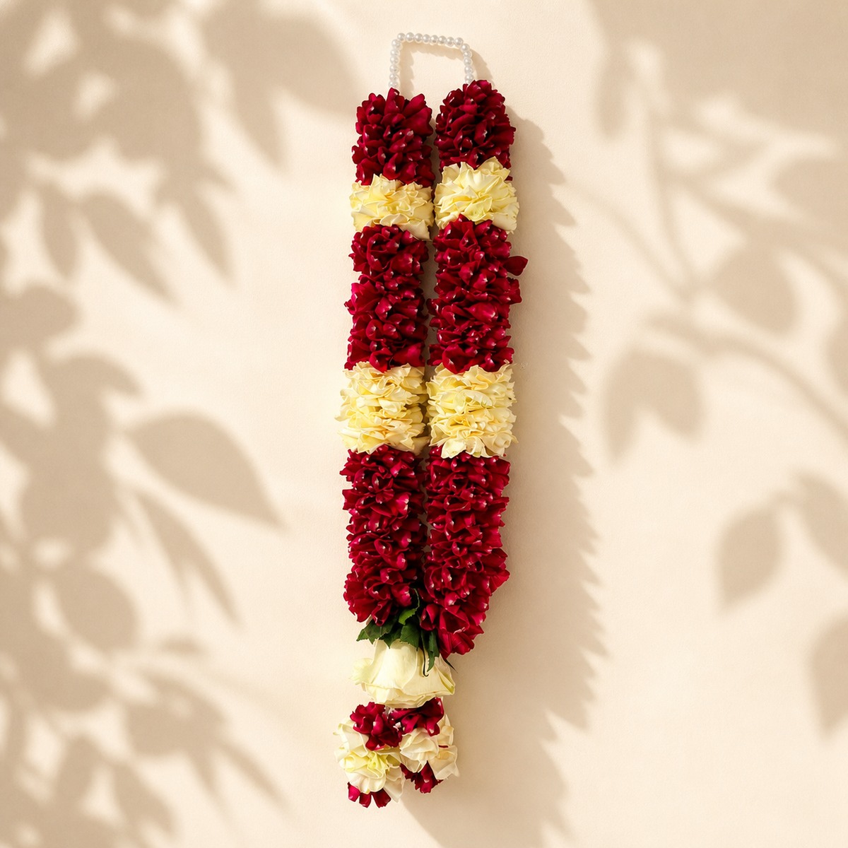Burgundy and ivory rose garland with pearl loop on warm ivory leaf-shadow backdrop