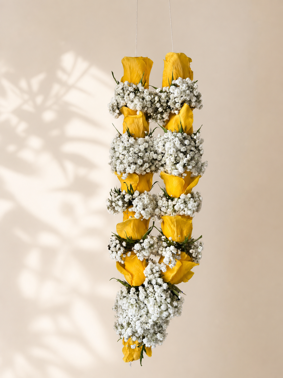 Golden yellow rose and white baby's breath hanging garland on ivory leaf-shadow backdrop